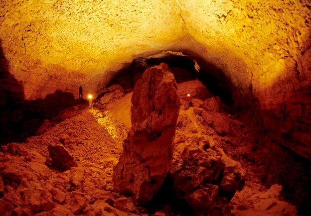 A caver standing in an illuminated cave the size of a cathedral