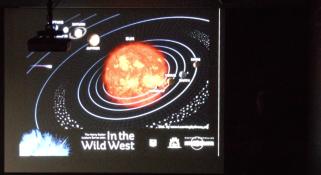 A slide from Alex Bevan's presentation who is standing to the right but in total darkness